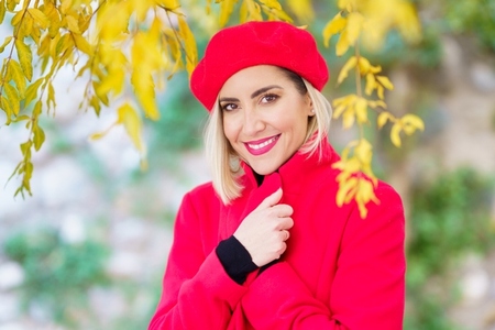 Fashionable smiling lady adjusting coat collar in autumn forest