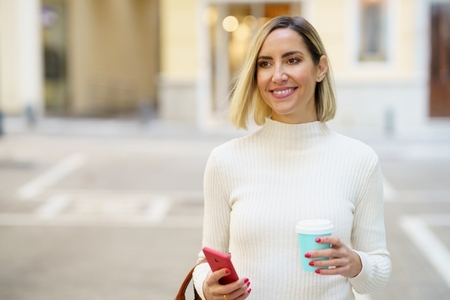 Smiling woman with takeaway coffee and smartphone on street
