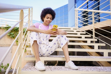 Black woman browsing smartphone on staircase