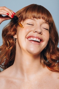 Smiling woman applying face serum with a dropper in a studio