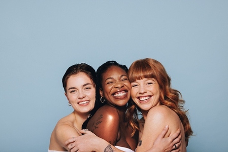 Three women with different skin tones embracing each other