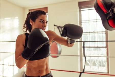 Female boxer punching focus pads in a boxing ring