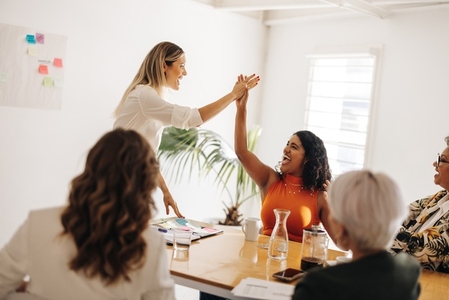 Successful businesswomen high fiving each other in a boardroom