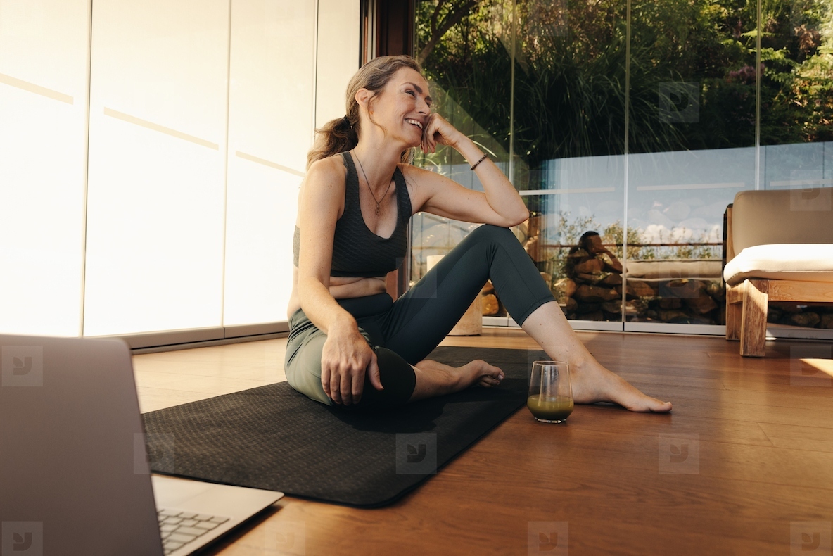 Happy senior woman sitting in front a laptop on a yoga mat