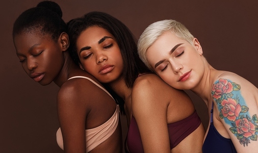 Portrait of three diverse women in lingerie standing together with eyes closed against a brown background