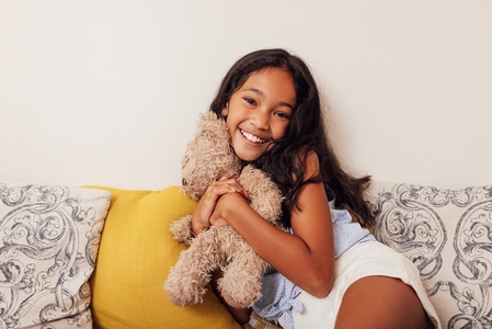 Girl with toy on the sofa  Smiling kid hugging a teddy bear and looking at camera