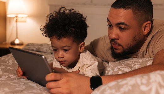 Father and son looking at digital tablet while lying on bed in evening