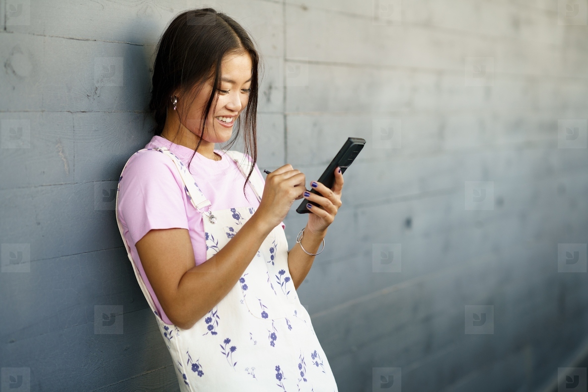 Positive Asian woman using her smartphone with a pen or stylus  outdoors