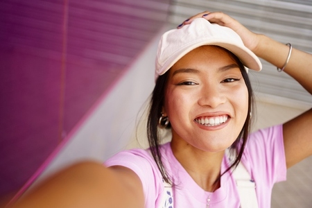 Cheerful Asian woman taking selfie on street