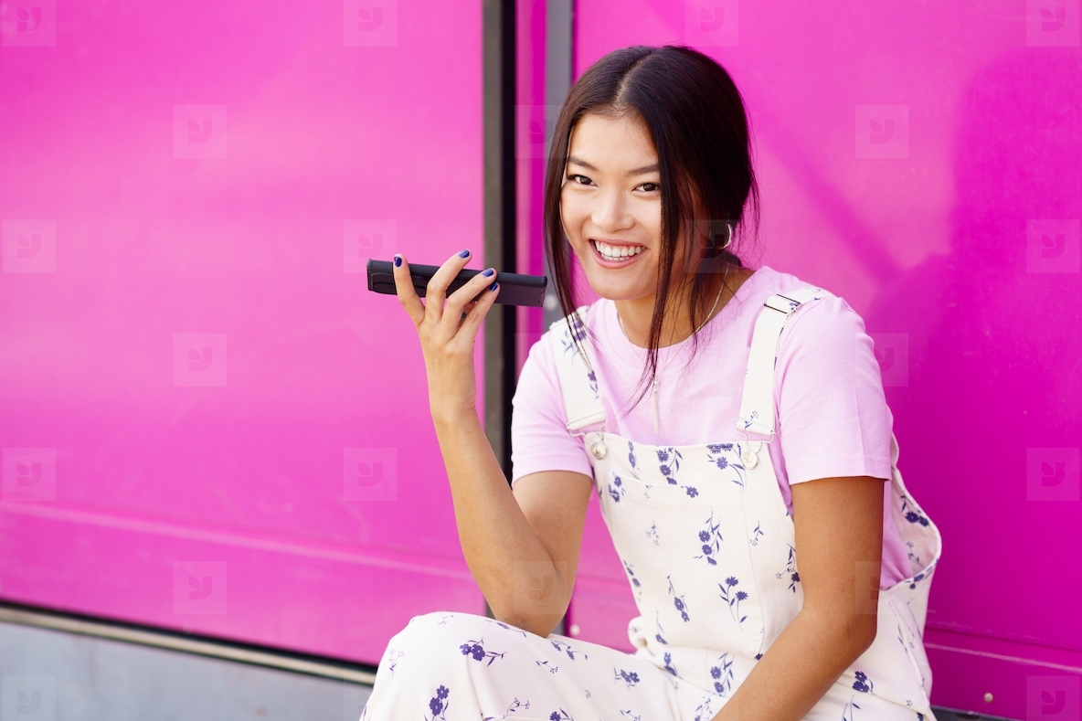 Cheerful Asian young woman using recording a voice note in her smartphone