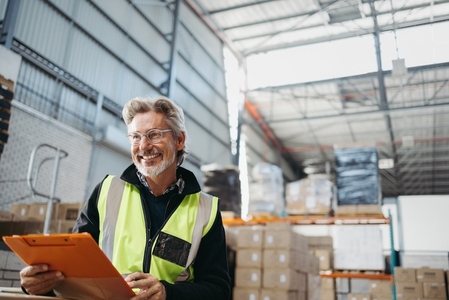 Senior warehouse supervisor smiling happily while holding a clipboard