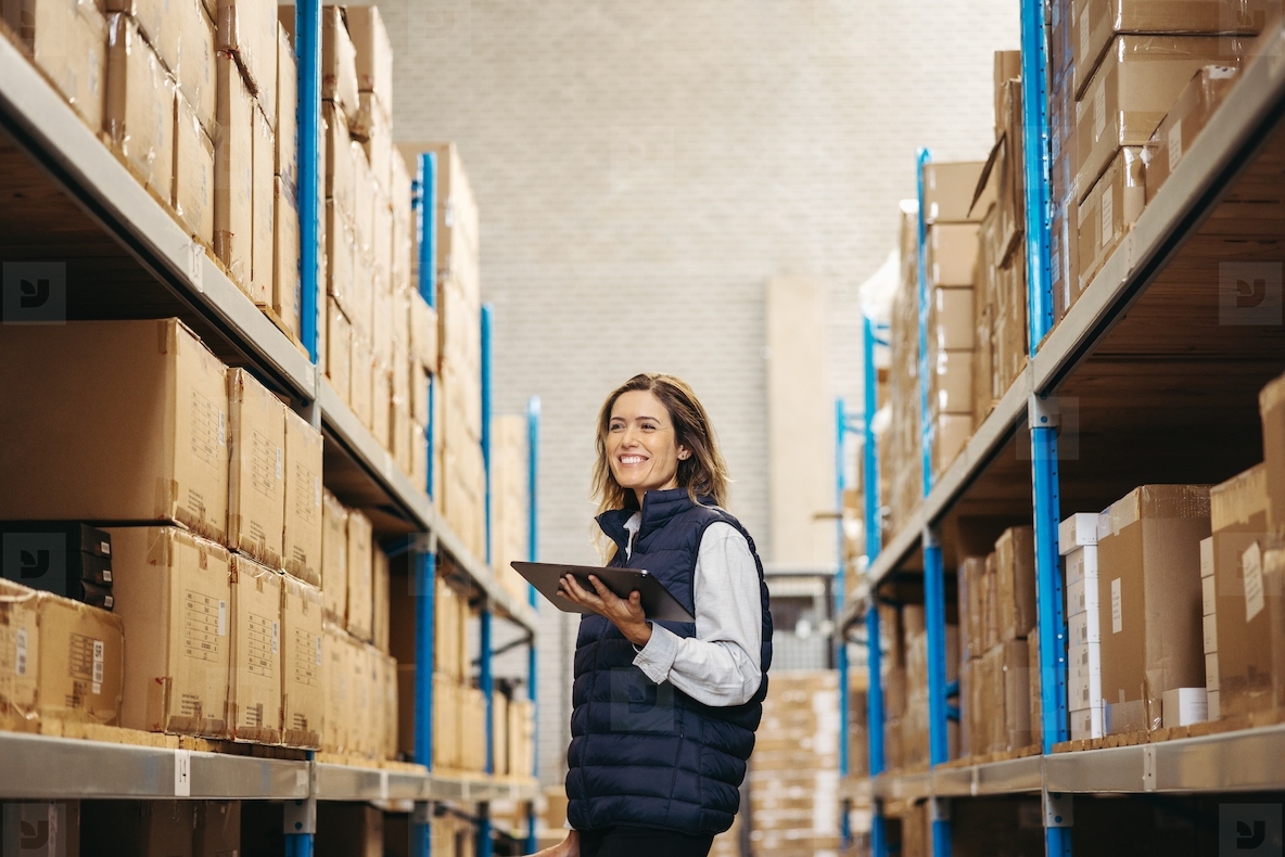 Happy young woman doing stock control in a warehouse