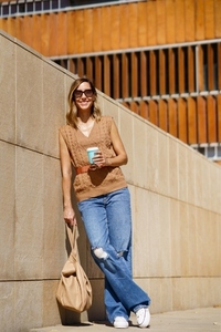 Stylish female with coffee leaning on wall