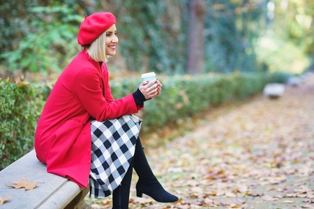 Smiling woman with takeaway drink sitting in park