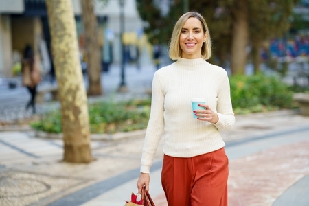 Smiling woman with cup of beverage carrying paper bag