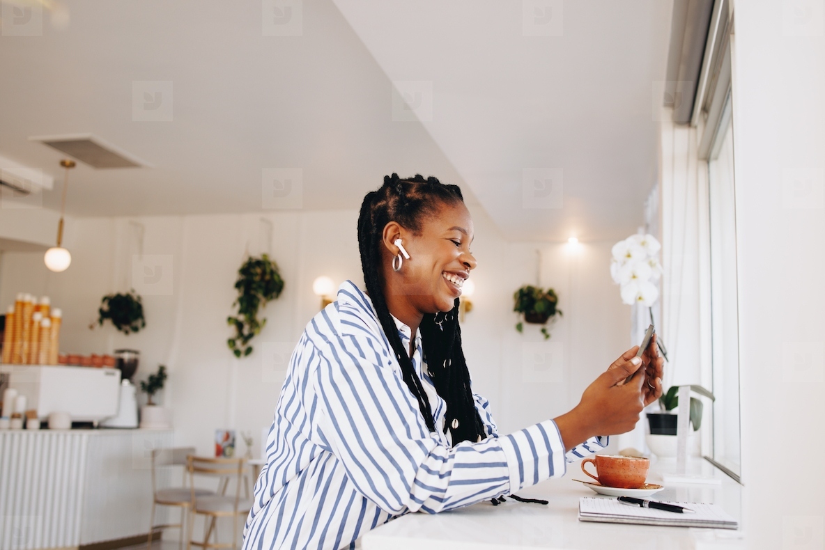 Cheerful young businesswoman having a video call on a smartphone while working in a coffee shop