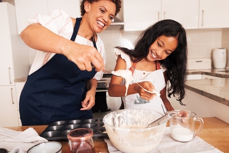 Girl and her grandmother are having fun while mixing dough in the kitchen  Smiling granny and a kid cooking together