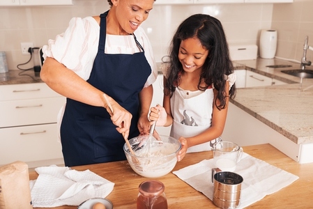 Mature woman teaching a girl to make dough  Smiling grandmother and kid mixing batter
