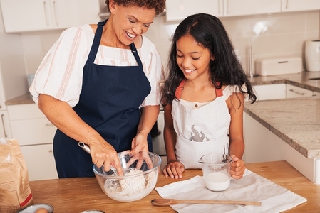 Grandmother mixing dough in a bowl while granddaughter watching