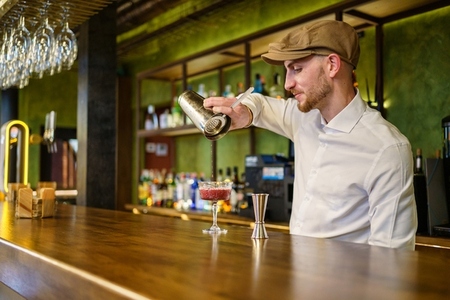 Bearded bartender preparing cocktail in pub