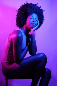 Positive black woman under neon light with eyes closed