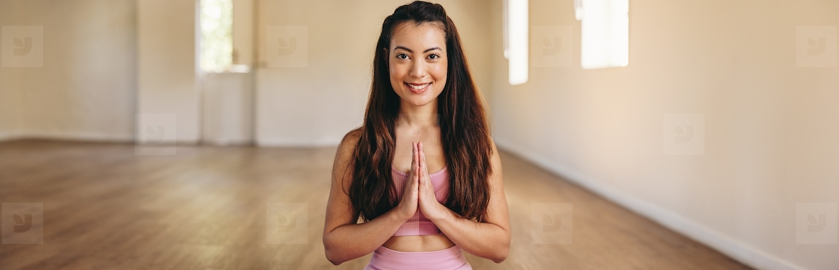 Cheerful young woman smiling at the camera while meditating in prayer pose in a yoga studio