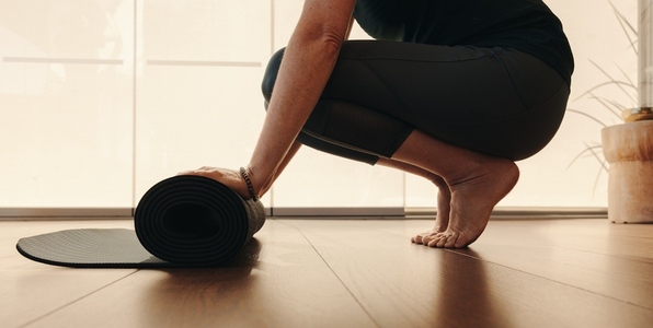 Senior woman rolling up a yoga mat at home