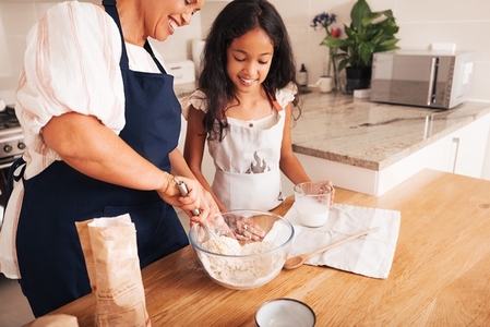 Mature woman showing her granddaughter how to mixing a dough