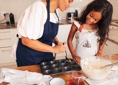 Grandmother teaching her granddaughter how to make cupcakes pouring batter in moulds
