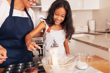 Smiling girl scoops batter from a bowl