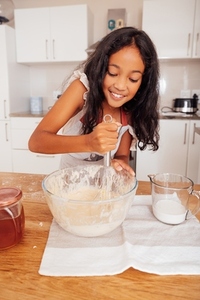 Smiling girl mixing a dough  Cheerful kid making dough for cupcakes in the kitchen