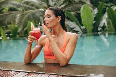 Young woman drinking cocktail in swimming pool