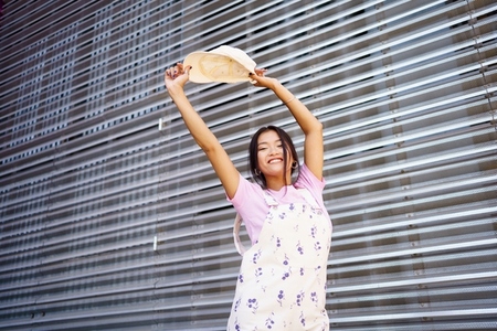 Cheerful Asian female raising arms with cap