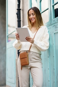 Positive female in stylish clothes browsing tablet on street