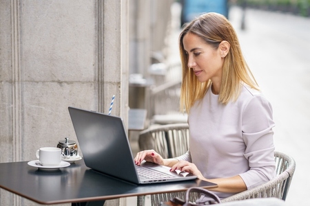 Focused female remote worker using laptop on cafe terrace