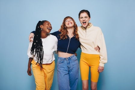 Three best friends laughing happily while embracing each other in a studio