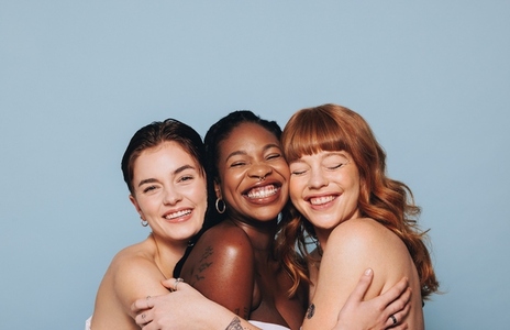 Group of happy women with different skin tones smiling and embracing each other in a studio