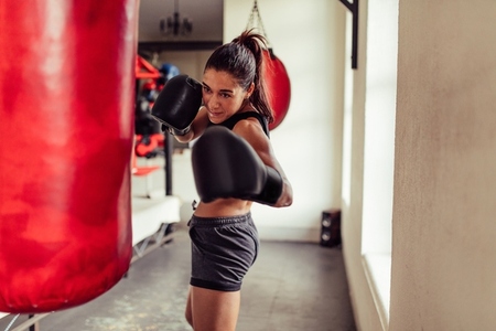Fit female boxer punching a red bag in the gym
