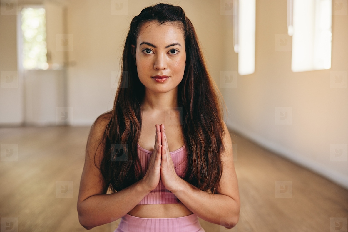Young woman looking at the camera while meditating in prayer pose in a yoga studio
