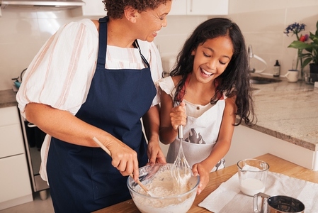 Happy girl and her grandma mixing dough in a glass bowl in a kitchen