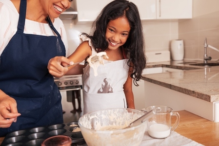 Granny and granddaughter cook together  Happy girl holding a spoon with dough on it
