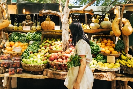 Side view of a young woman with a bag looking at vegetables and fruits at a local outdoor market