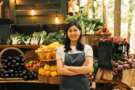 Portrait of a confident outdoor market employee  Smiling Asian woman in an apron standing at her outdoor stall