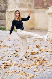 Cheerful young woman kicking fallen leaves while walking in park