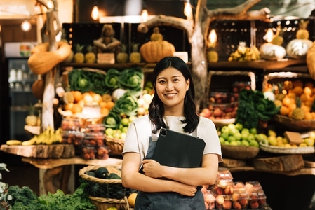 Smiling entrepreneur holding a digital tablet standing at an outdoor market  Asian woman in an apron looking at camera while standing against a street food market