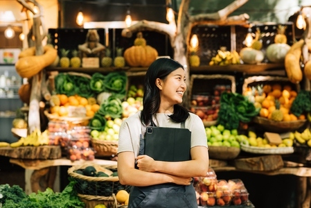 Smiling businesswoman standing at an outdoor market  Female vendor in apron holding digital tablet