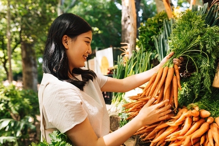 Smiling buyer holding a bunch of carrots  Asian woman choosing vegetables in the local market