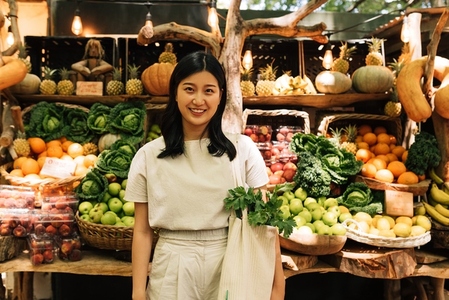 Portrait of an Asian woman standing on an outdoor market  Female with a shopping bag standing at a stall with organic food
