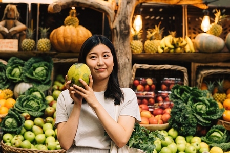 Asian woman holding a melon while standing at an outdoor market