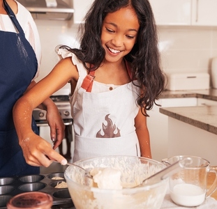 Smiling girl holding a spoon with batter while standing in kitchen